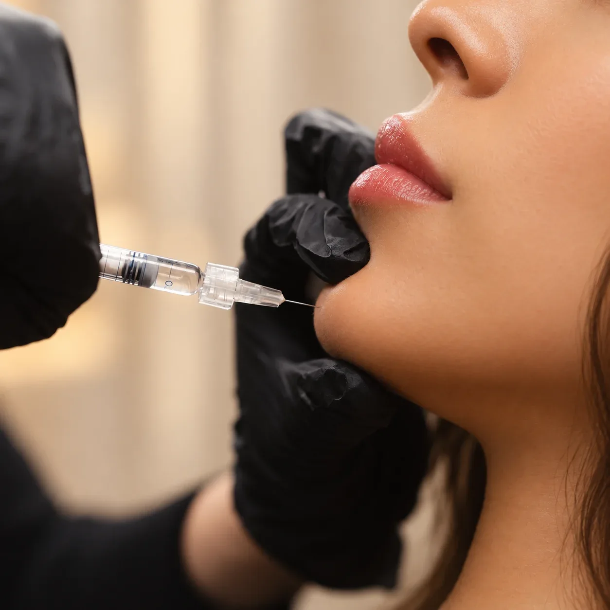 Black-gloved hands position a fine injection needle at a reclining woman's chin.