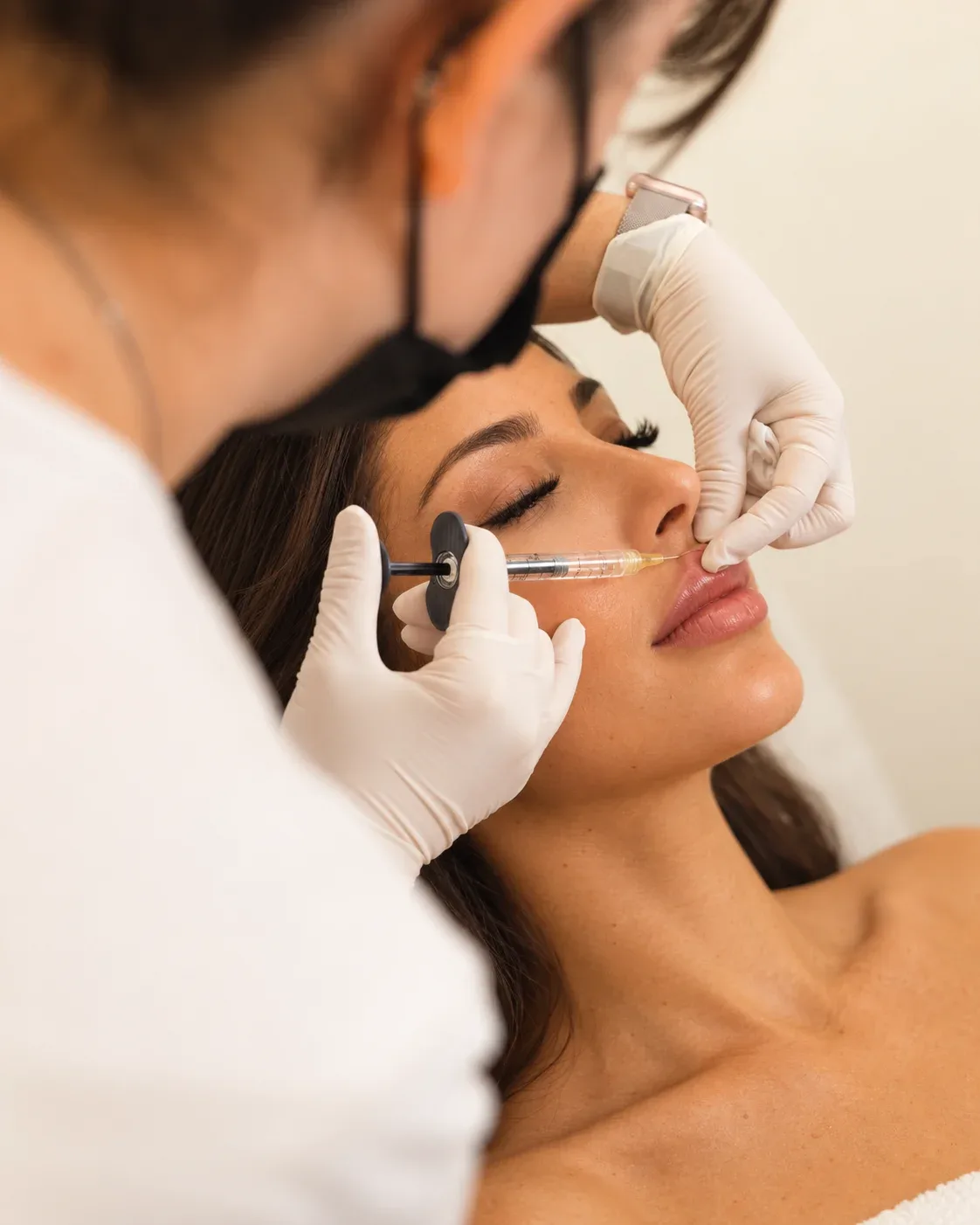 Lip filler injection with a fine needle and white-gloved hands supporting the upper lip